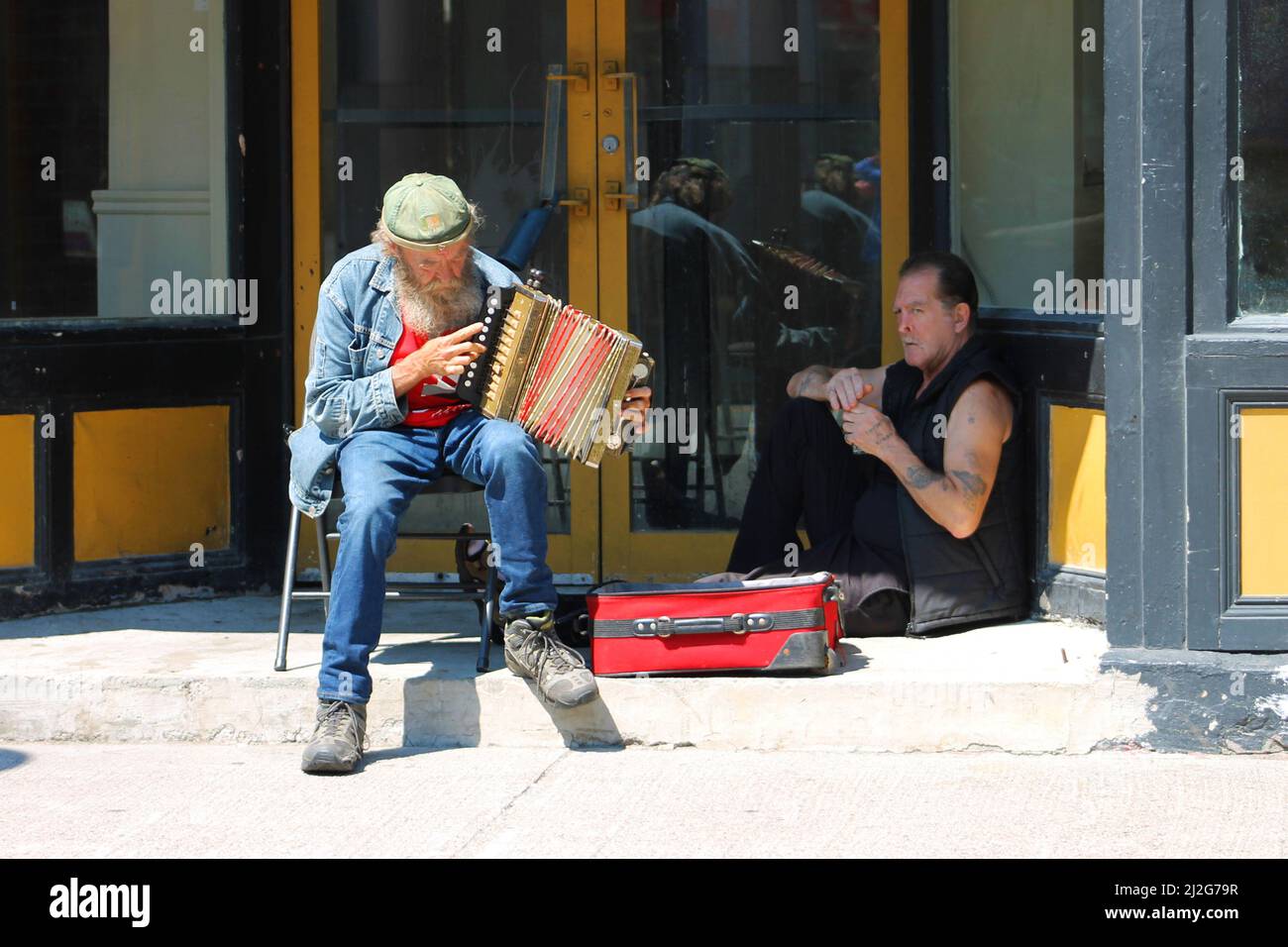 Ein Straßenmusiker, der ein Akkordeon in einer Tür spielt, ein Straßenmensch sitzt ebenfalls in der Tür, Water Street, St. John's, NL Stockfoto