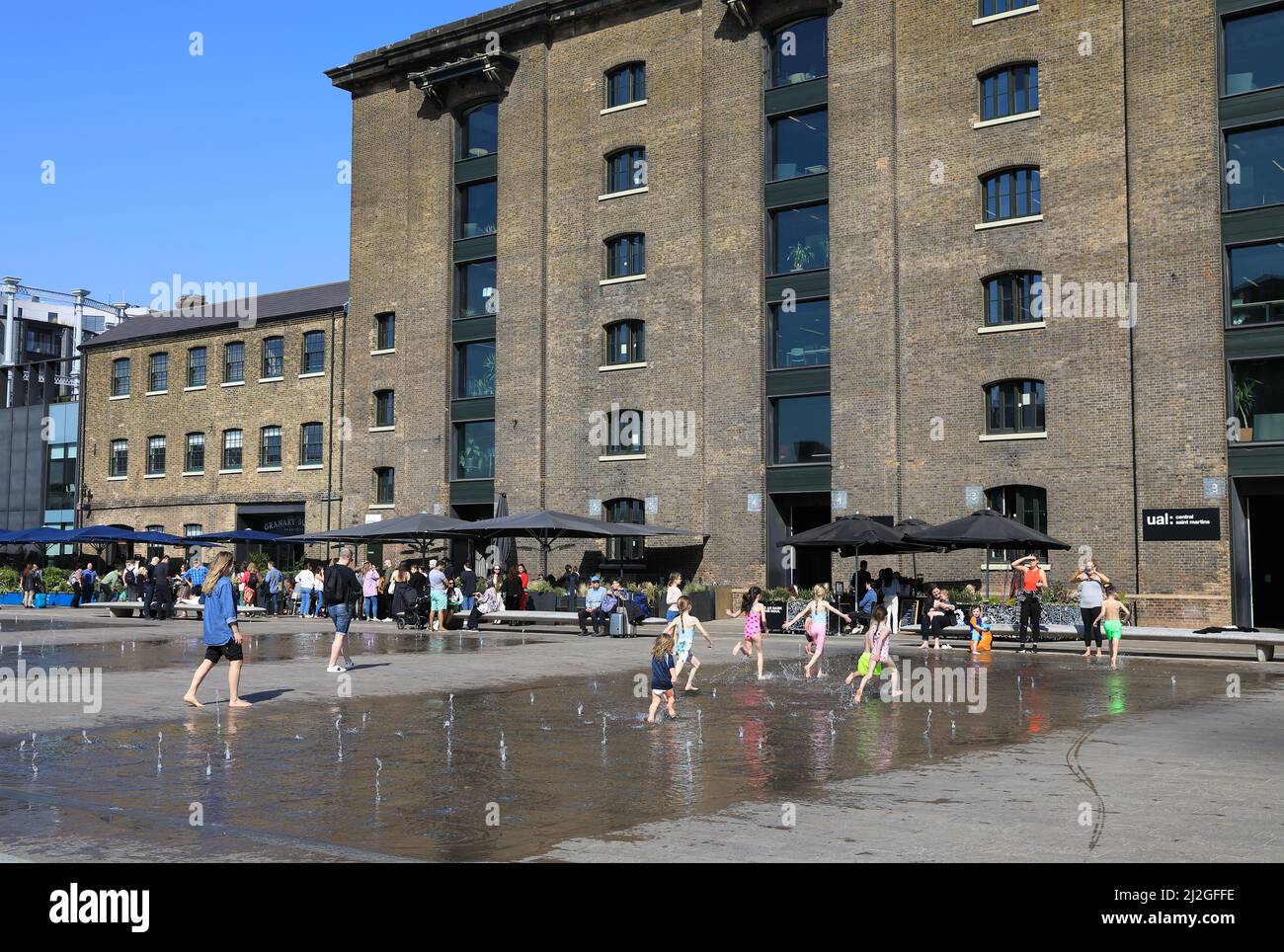 Kinder spielen in der Frühlingssonne in den Springbrunnen des Granary Square in Kings Cross, Nord-London, Großbritannien Stockfoto