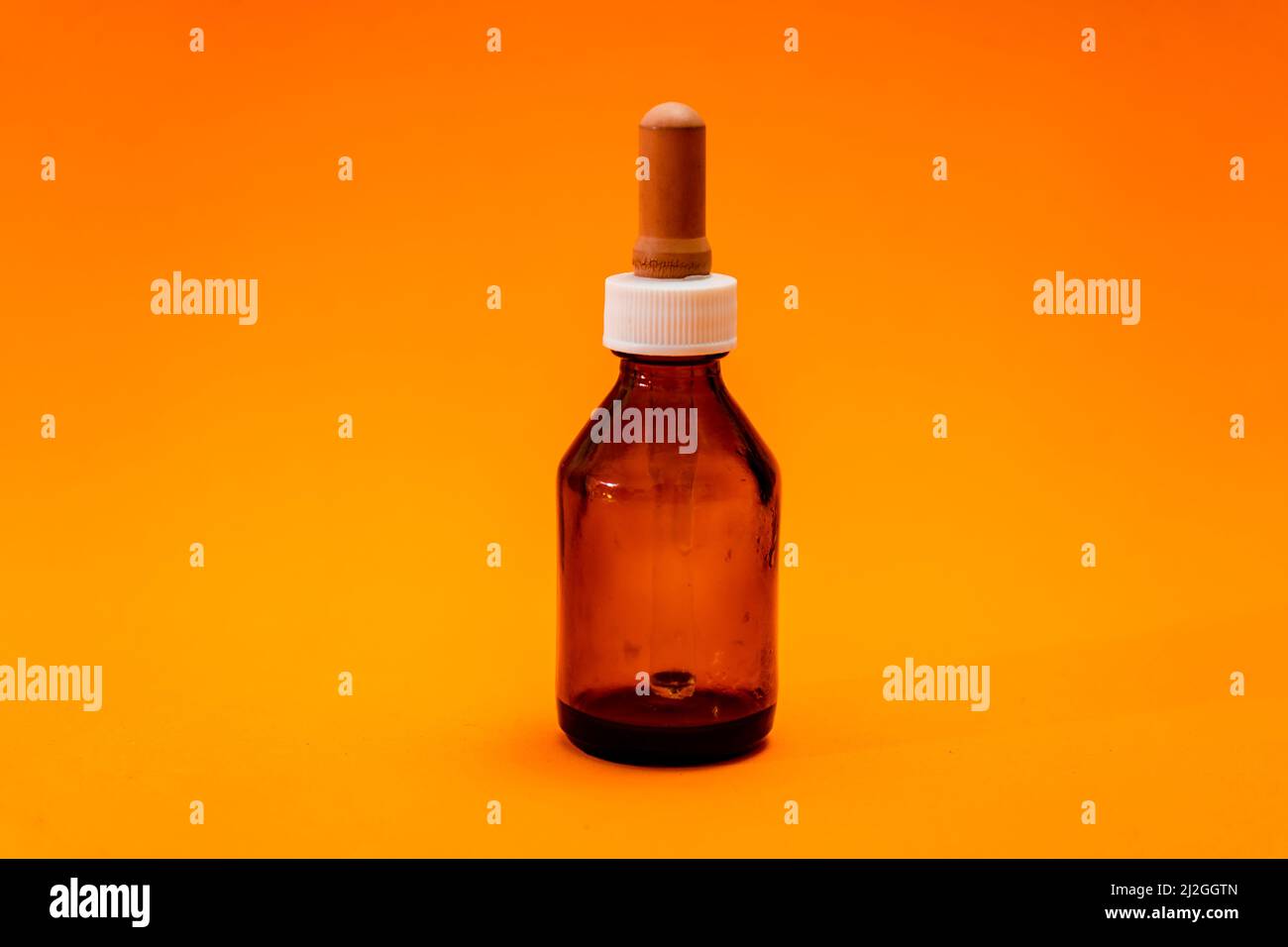 Kleine Flasche mit bernsteinfarbenem Glastropfer isoliert auf orangefarbenem Hintergrund. Platz zum Kopieren. Stockfoto
