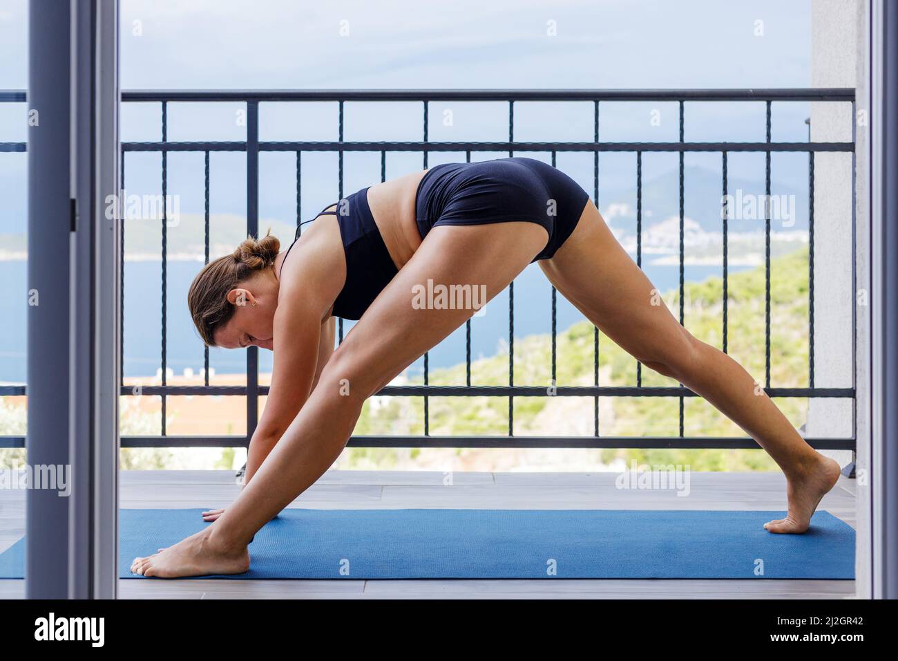 Junge Fitness-Frau macht morgens Yoga-Praxis auf dem Balkon in der Nähe des Meeres Stockfoto