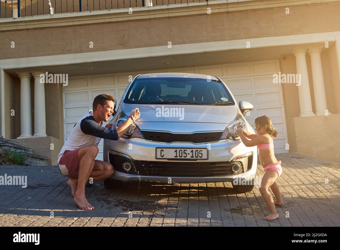 Vaterschaft und Kindheit. Aufnahme eines Vaters und einer Tochter, die Spaß beim Waschen eines Autos haben. Stockfoto