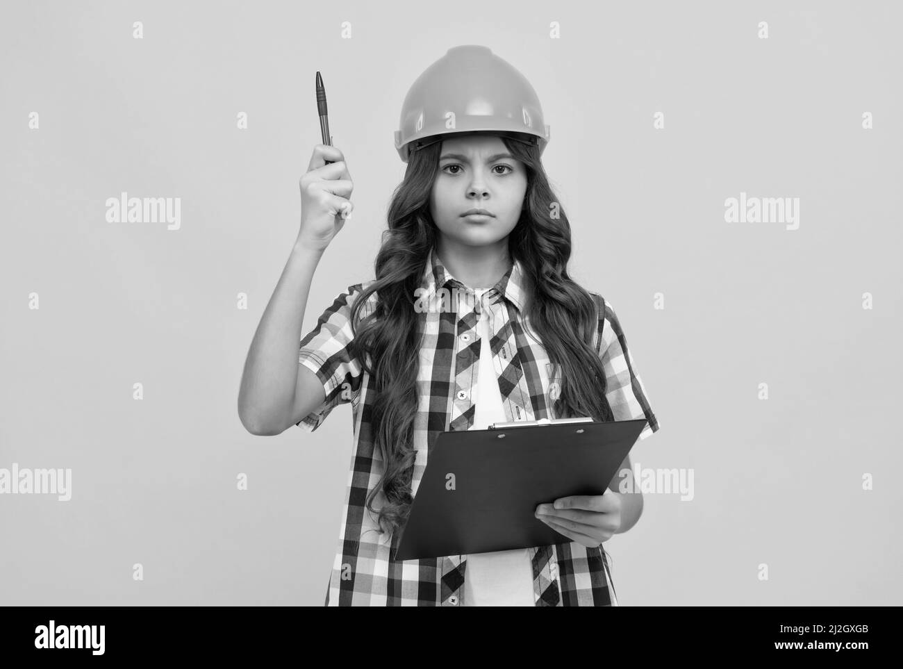 Ernsthaftes Kind im Bauhelm, das mit Klemmbrett arbeitet, unter Kontrolle Stockfoto