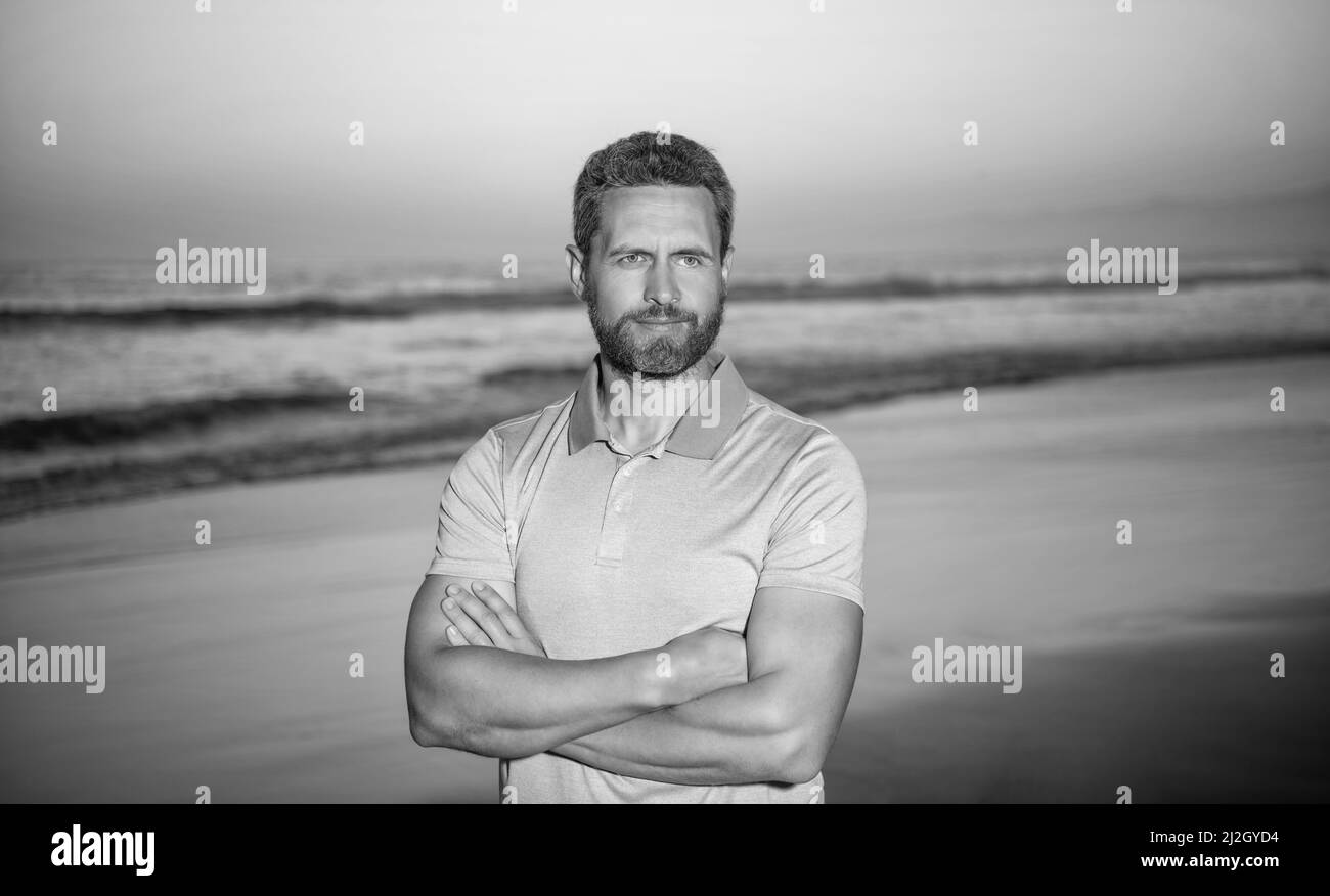 Sommerurlaub. Schöner Mann mit Bart im Sonnenuntergang über dem Meer. Unrasiert Kerl am Morgen Strand Stockfoto