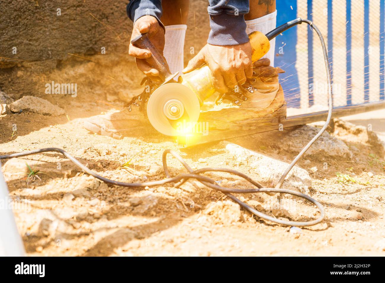 Nahaufnahme der Hände eines lateinischen Arbeiter mit blauem Kragen, der eine tragbare Kreissäge zum Schneiden eines Rohrs verwendet Stockfoto