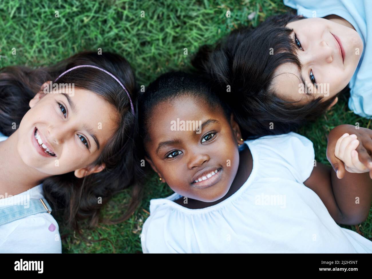 Es war ein lustiger Tag. Aufnahme von drei entzückenden Kindern, die zusammen auf dem Rasen liegen. Stockfoto