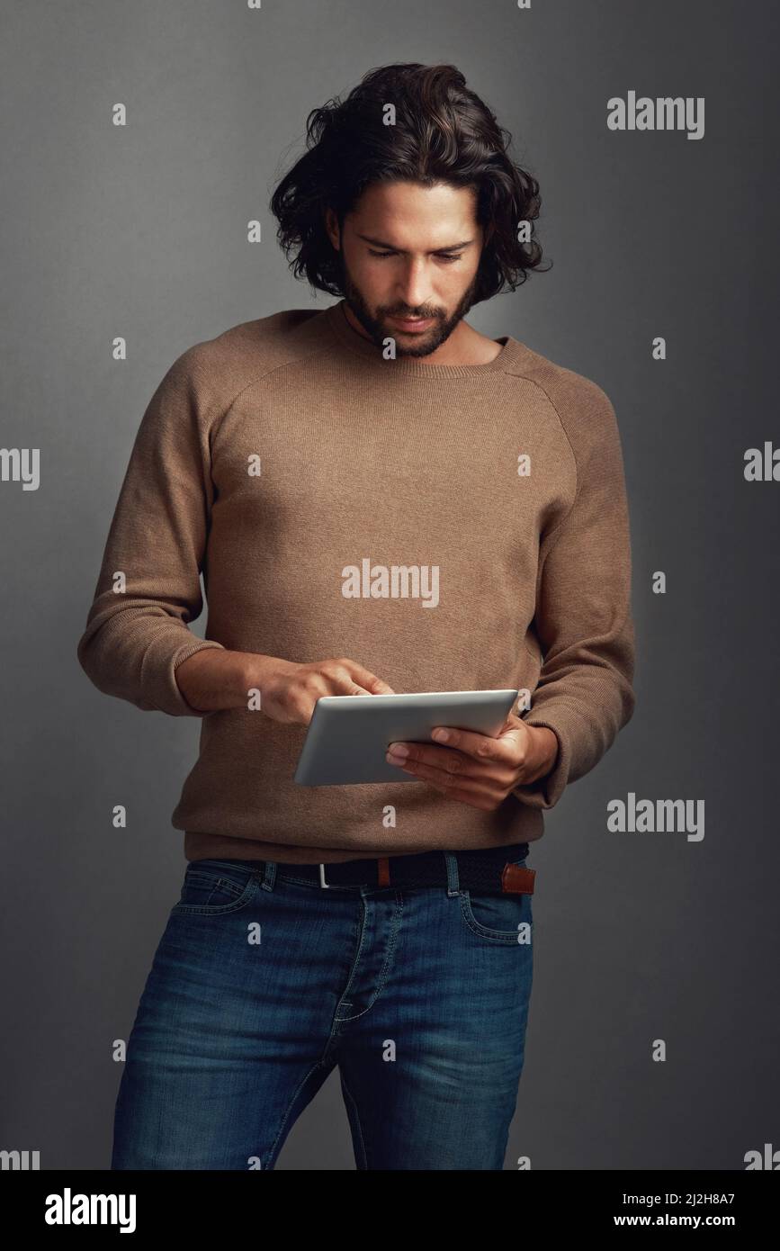 Es gibt buchstäblich eine App für alles. Studioaufnahme eines hübschen jungen Mannes mit einem digitalen Tablet vor grauem Hintergrund. Stockfoto