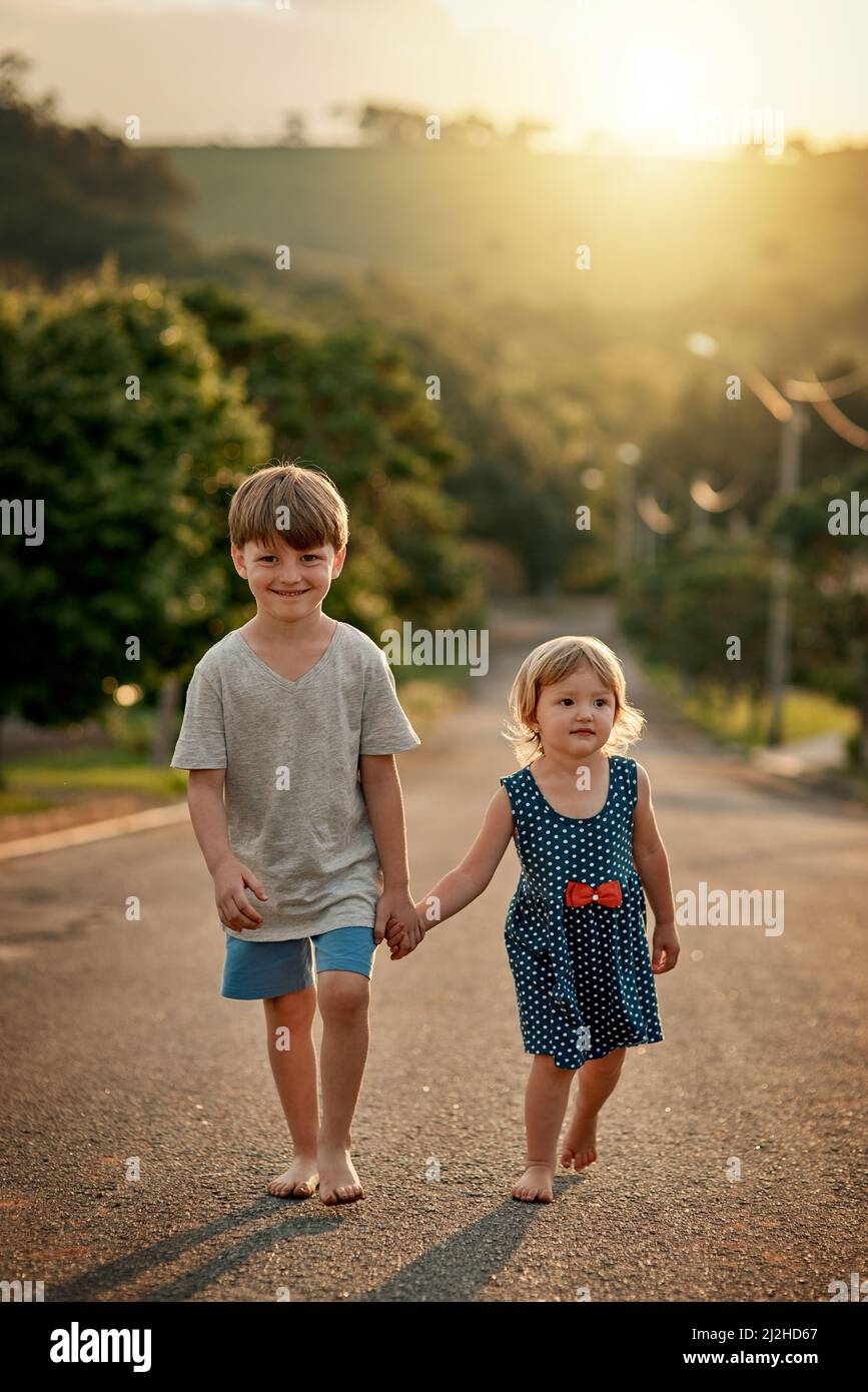 Mit meiner Schwester durch den Vorort schlendern. Aufnahme eines entzückenden kleinen Jungen, der Hand in Hand mit seiner Schwester die Straße runter in der Nachbarschaft läuft. Stockfoto