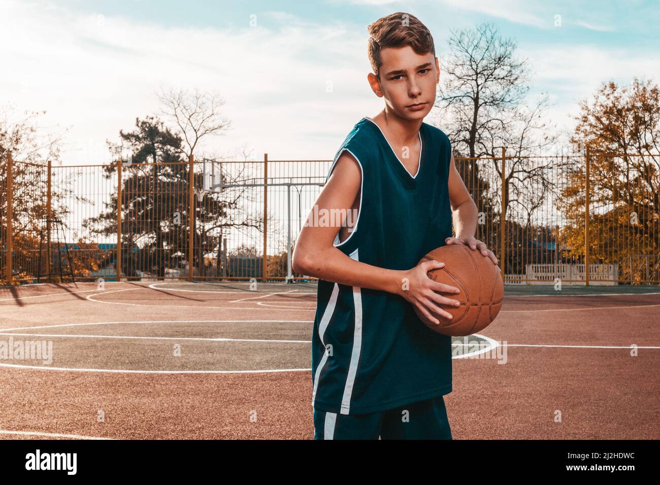 Sport und Basketball. Ein junger Teenager in einem blauen Trainingsanzug  posiert mit einem Basketball in den Händen. Im Hintergrund ein  Basketballplatz. Horizontal. C Stockfotografie - Alamy