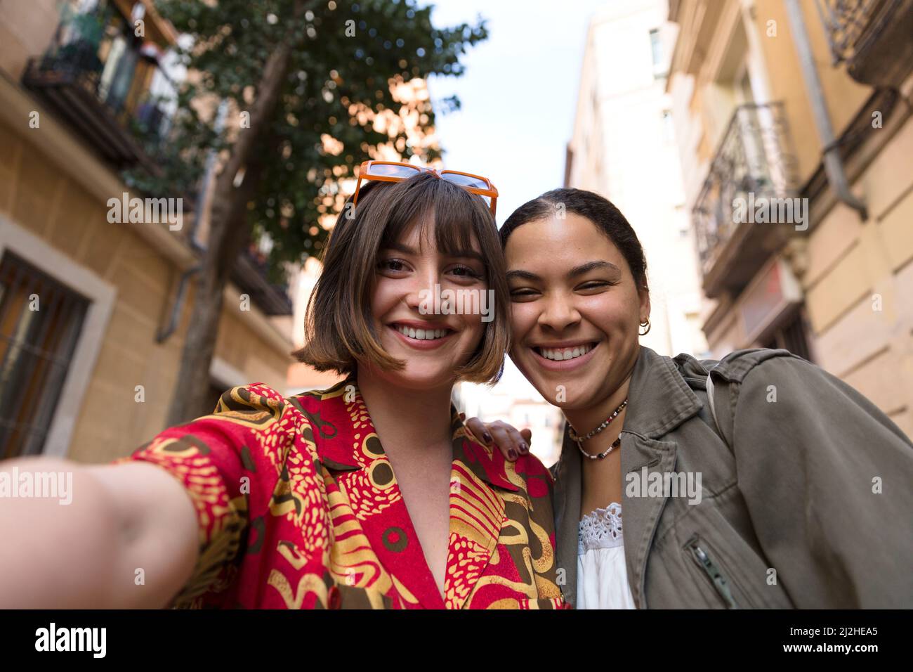 Zwei lächelnde Mädchen, die zusammen mit dem Mobiltelefon im Freien ein Foto machen. Glückliche multiethnische Menschen. Stockfoto