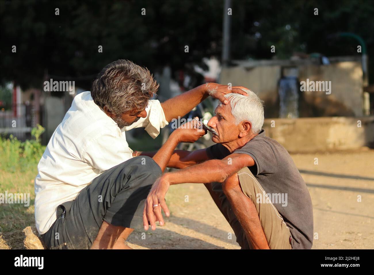 Pali Rajasthan, Indien-November 01 , 2021.Foto eines indischen erwachsenen Barbiers sitzt draußen im Dorf macht einen älteren Mann die Ersparnisse (rasieren) in t Stockfoto