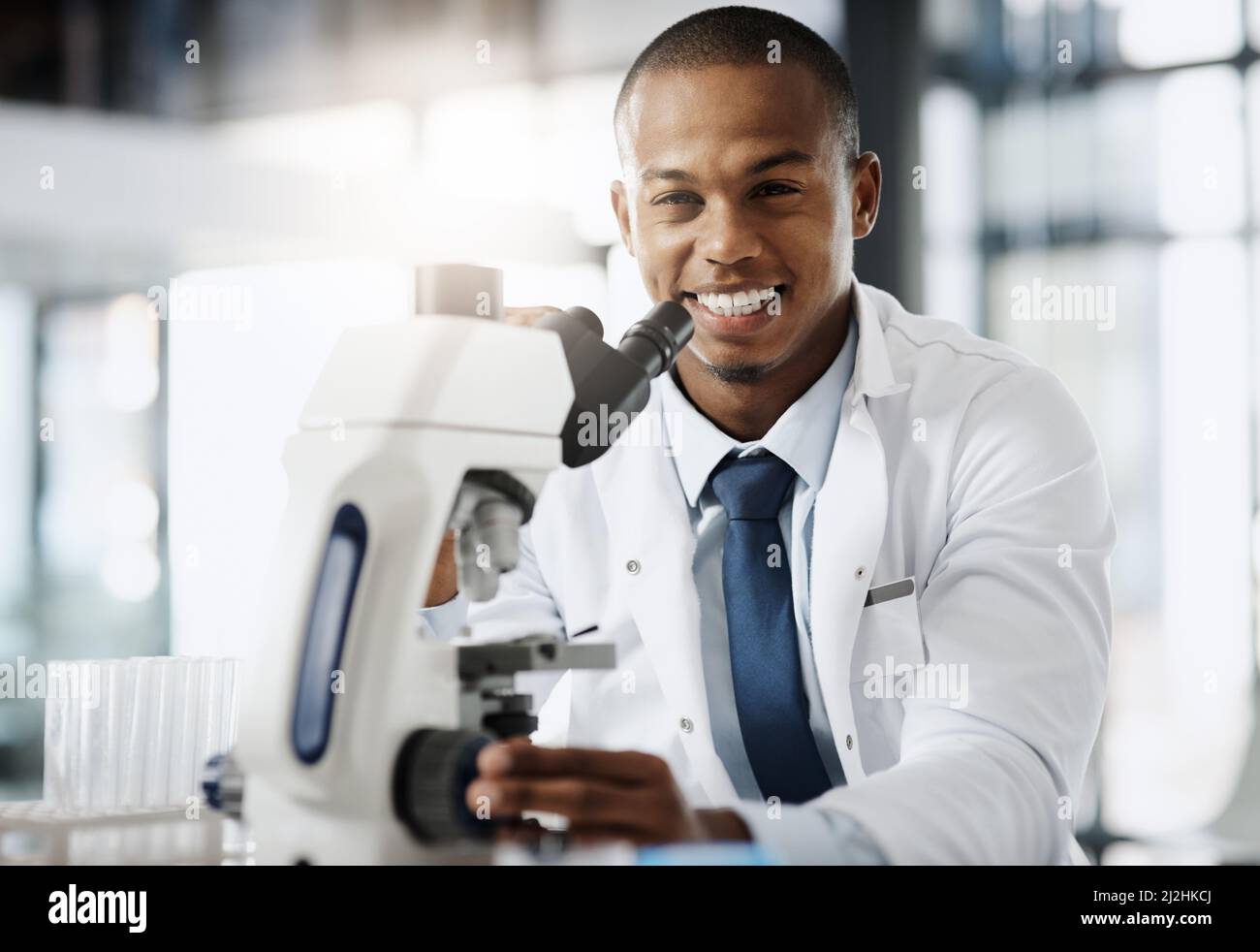 Die Welt verändern eine Entdeckung nach der anderen. Beschnittenes Porträt eines hübschen jungen Wissenschaftlers, der ein Mikroskop benutzte, während er in seinem Labor forschte. Stockfoto