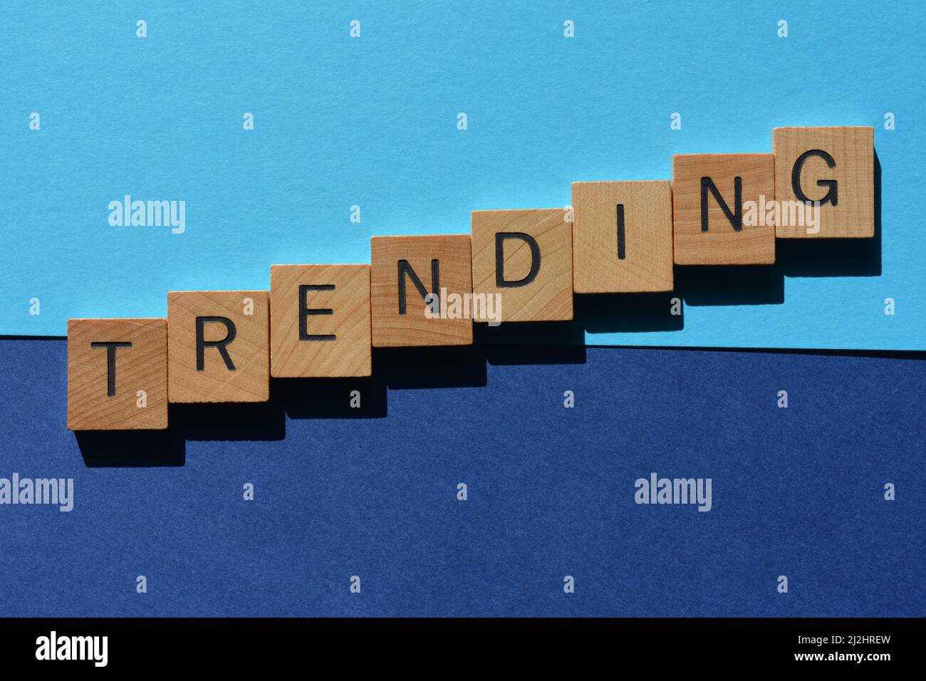 Trending, Wort in Holzalphabet Buchstaben isoliert auf blauem Hintergrund Stockfoto