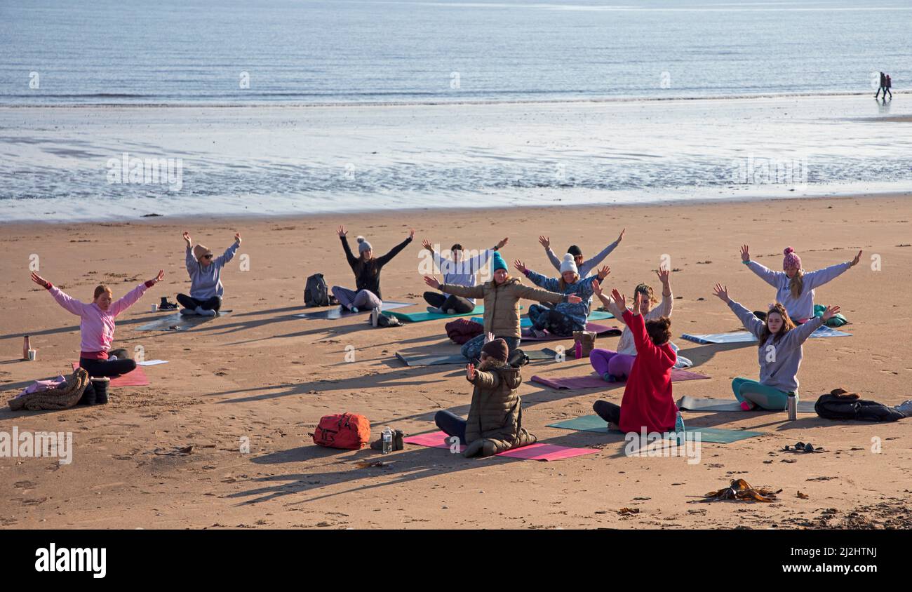 Portobello, Edinburgh Schottland, Großbritannien. April 2022. Erste Beach Yoga Klasse von 2022 am Meer neben dem Firth of Forth. Die Temperatur beträgt etwa 5 Grad Celsius, aber die Sonne gab der harten Gruppe Wärme. Stockfoto
