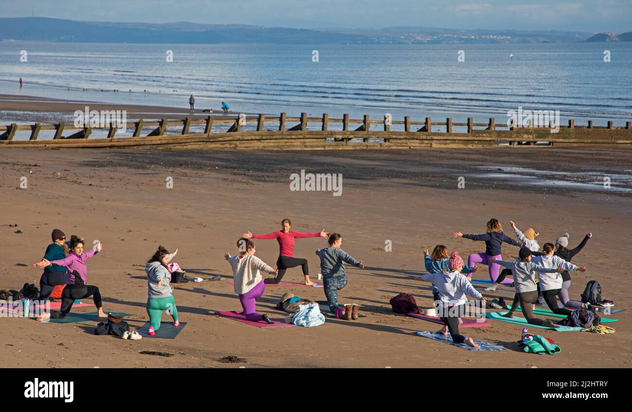 Portobello, Edinburgh Schottland, Großbritannien. April 2022. Erste Beach Yoga Klasse von 2022 am Meer neben dem Firth of Forth. Die Temperatur beträgt etwa 5 Grad Celsius, aber die Sonne gab der harten Gruppe Wärme. Stockfoto