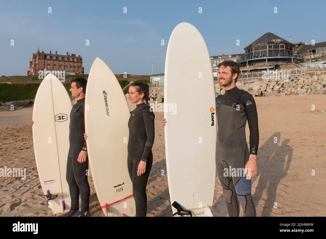 Eine Gruppe von Surfern, die ihre Surfbretter halten und am Fistral Beach stehen und auf das Meer in Newquay in Cornwall in Großbritannien blicken. Stockfoto