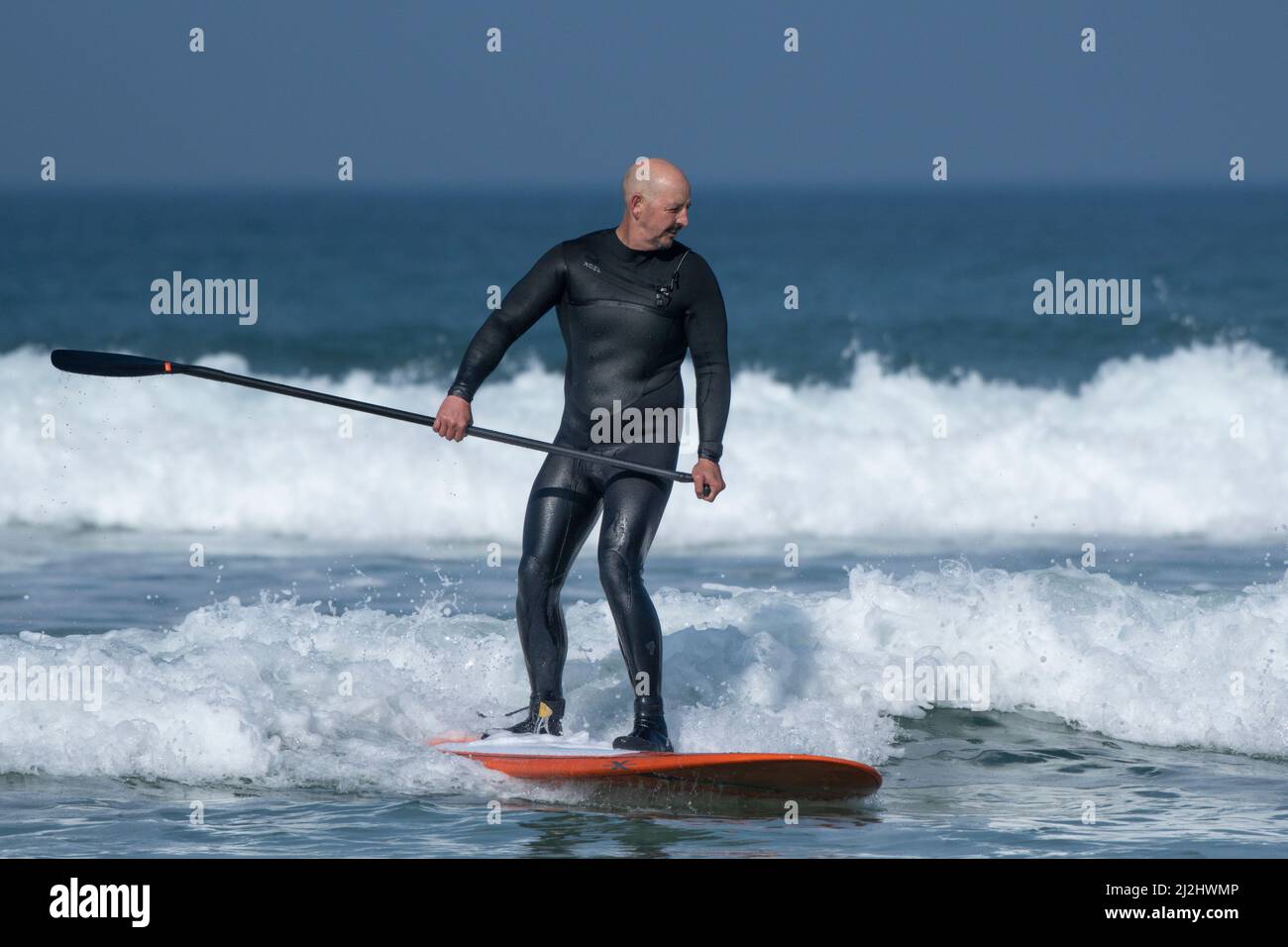 Ein reifer Paddle-Boarder auf einer Welle bei Fistral in Newquay in Cornwall in Großbritannien. Stockfoto