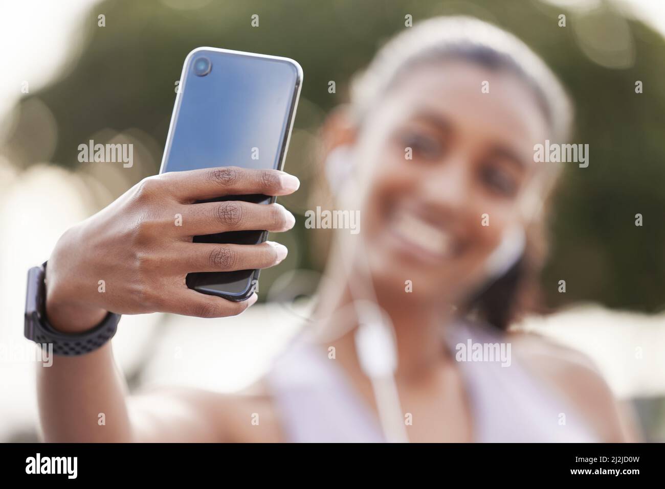 Ihr Telefon ist mit Fotos von ihrem Fortschritt gefüllt. Nahaufnahme einer sportlichen jungen Frau, die Kopfhörer trägt und Selfies macht, während sie im Freien trainiert. Stockfoto