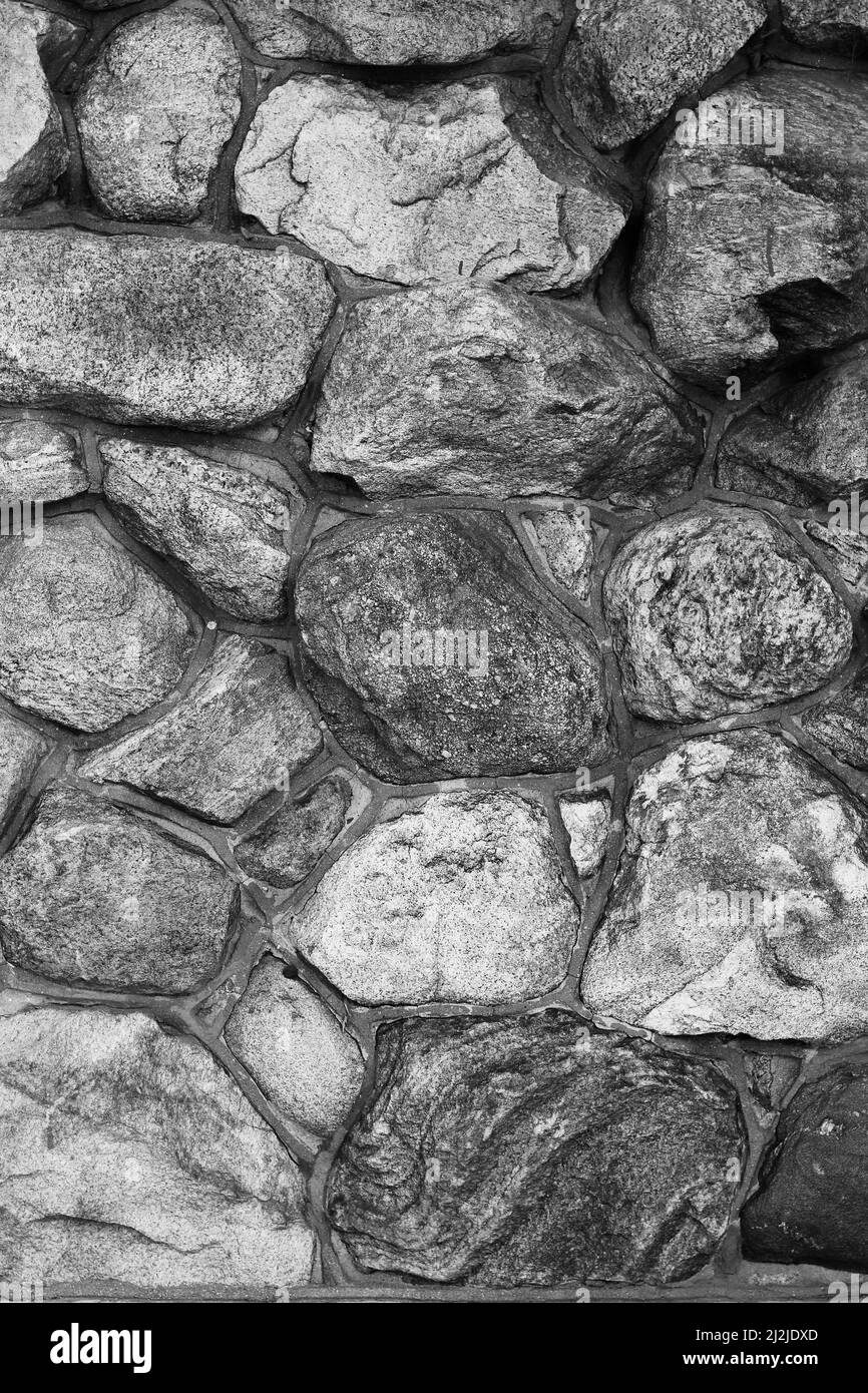 Rustikale Steinmauer mit runden Felsbrocken und Granitsteinen in schwarz-weißen Graustufen. Stockfoto