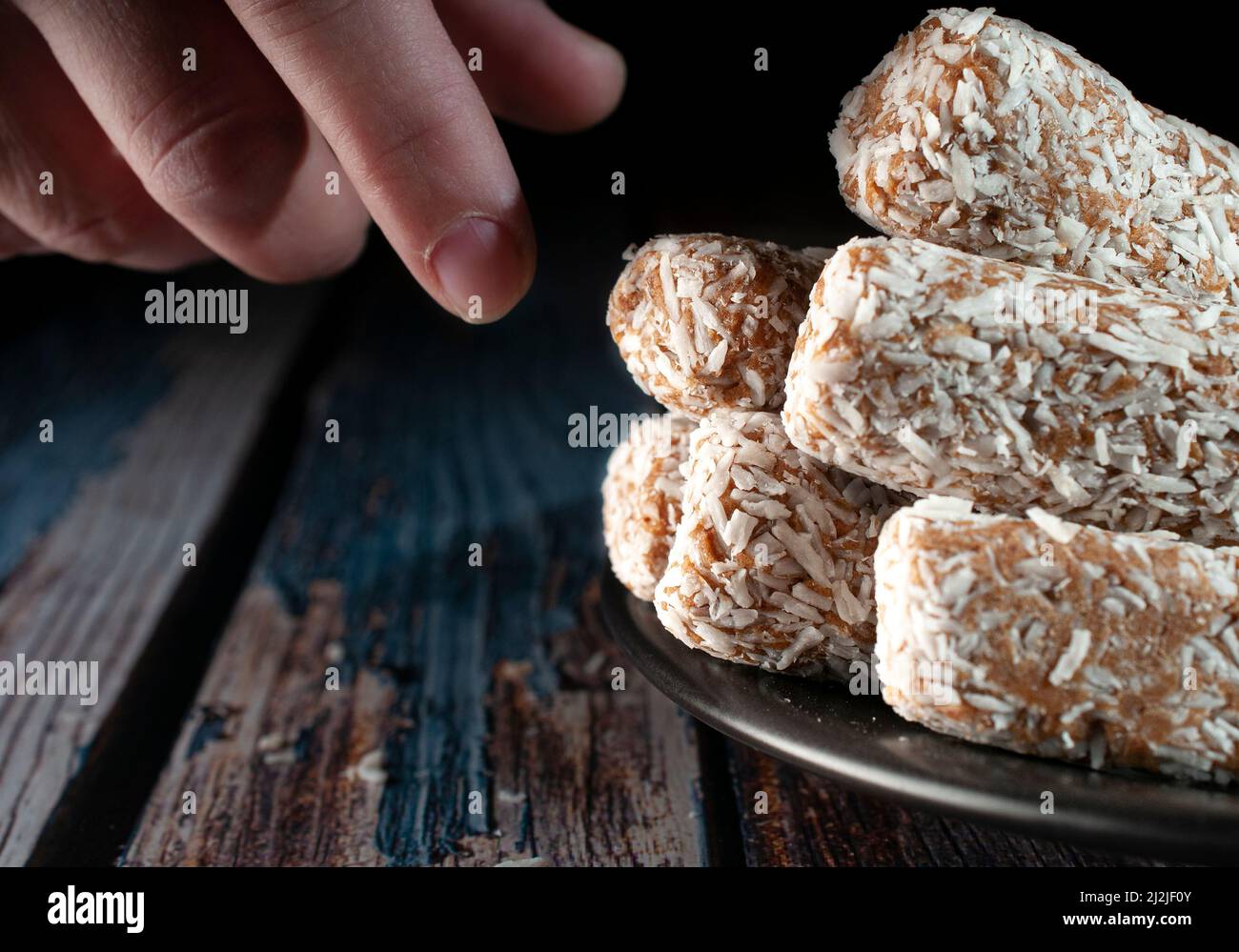 Bonbons, Datteln, die mit Kokosflocken bedeckt sind, auf einem schwarzen Teller über einem hölzernen Vintage-Tisch und einem dunklen Hintergrund Stockfoto