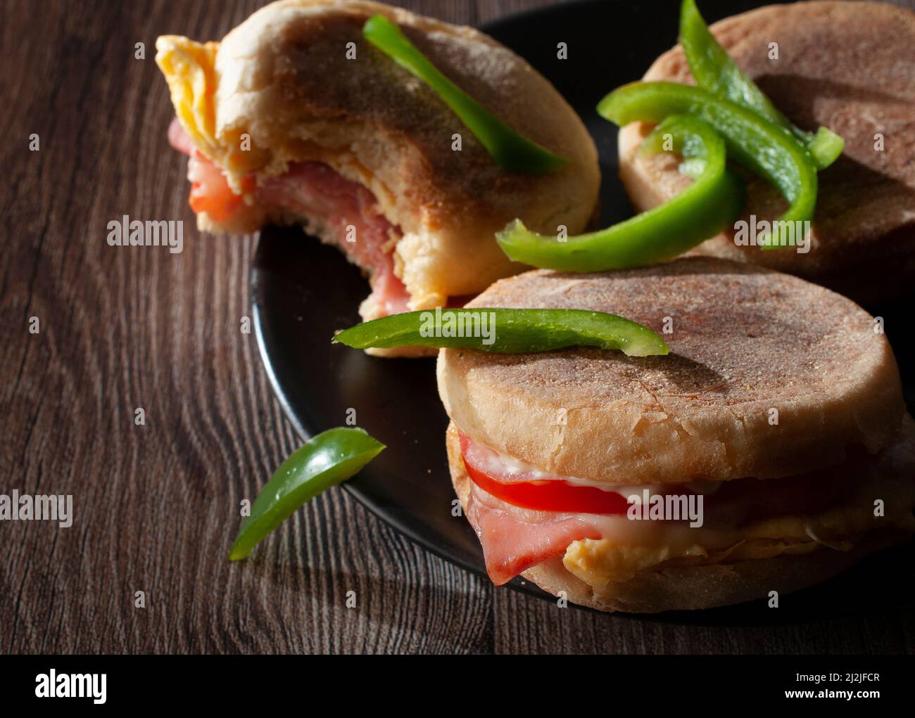 Frühstück Eier und Schinken englische Muffins mit Tomatenkäse und Mayo, mit Scheiben grüner Paprika, dunkle Food-Fotografie Stockfoto