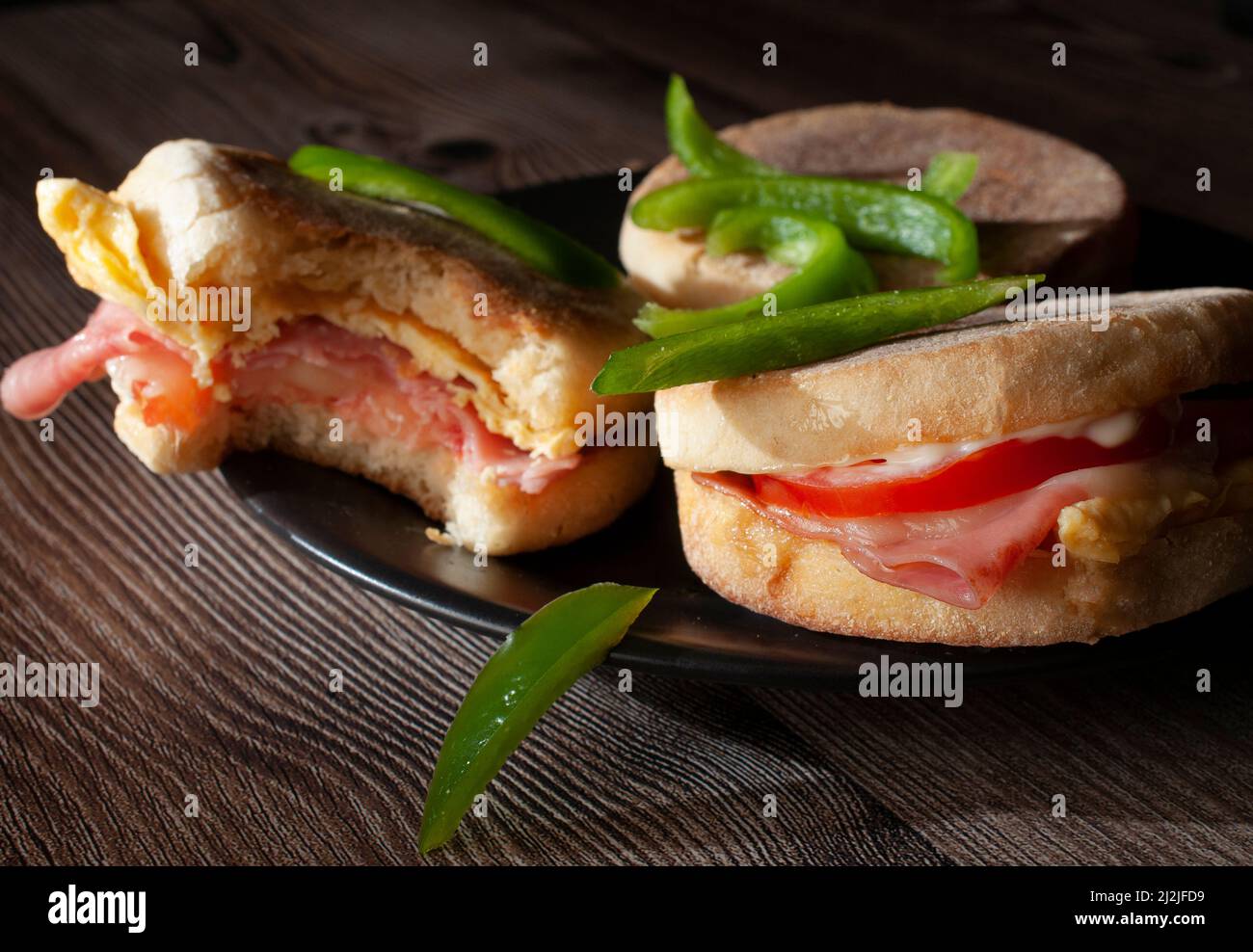 Frühstück Eier und Schinken englische Muffins mit Tomatenkäse und Mayo, mit Scheiben grüner Paprika, dunkle Food-Fotografie Stockfoto