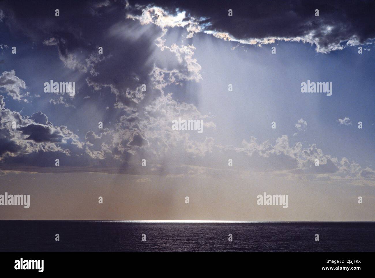 Helles Sonnenlicht, das durch den stürmischen Himmel über dem Meer scheint. Stockfoto