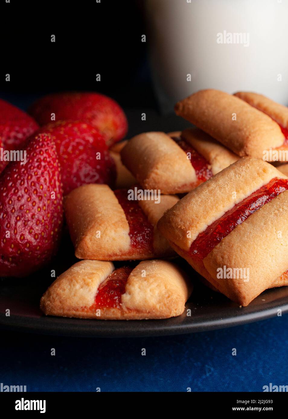Ein Stapel Erdbeer-Keks mit einem kalten Glas Milch und frischen natürlichen Erdbeeren auf der Seite dunkles Essen Stockfoto