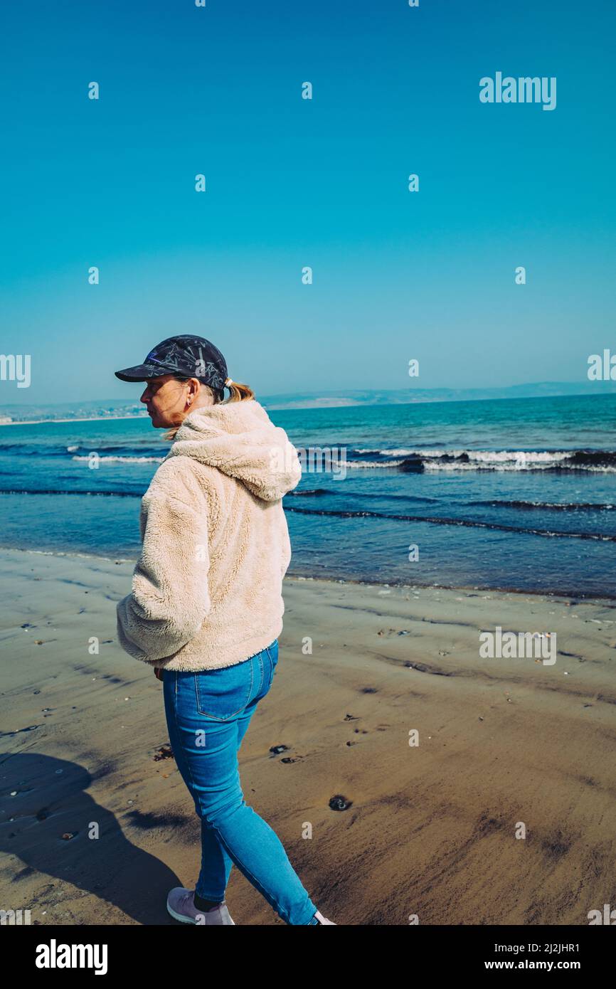 Frau mit Baseballmütze am Strand von Weymouth (Mar22) Stockfoto