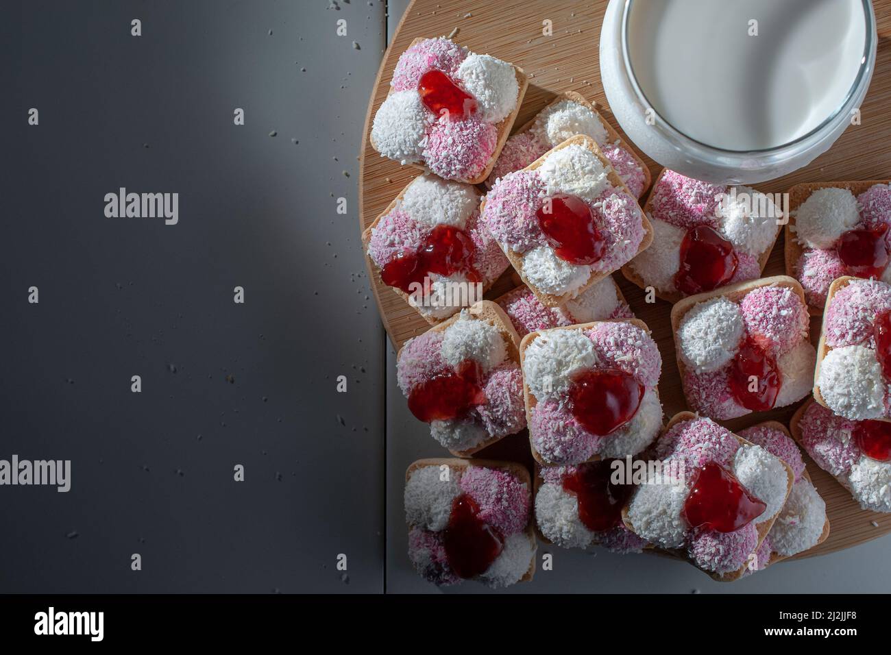 Kekse mit Lammfleisch, getrockneten Kokosflocken und Erdbeermarmelade, mit einem Glas eiskalter Milch auf der Seite Stockfoto