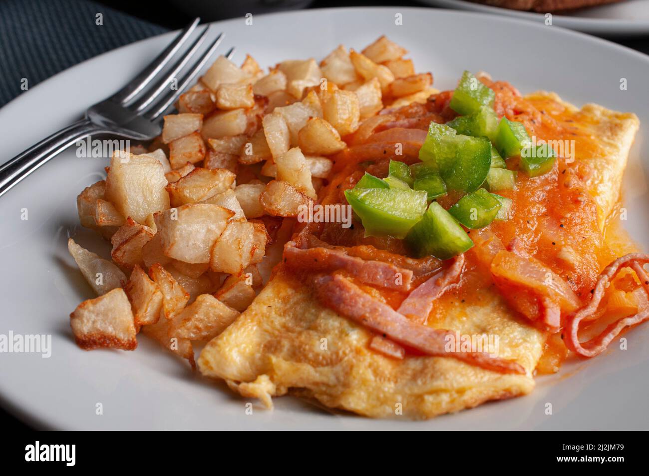 Omelette mit Käse, roten Tomaten und Zwiebel würzige Salsa und Würfel von grünen Paprika auf der Oberseite mit einer Seite von viereckigen frittierten Kartoffeln Stockfoto