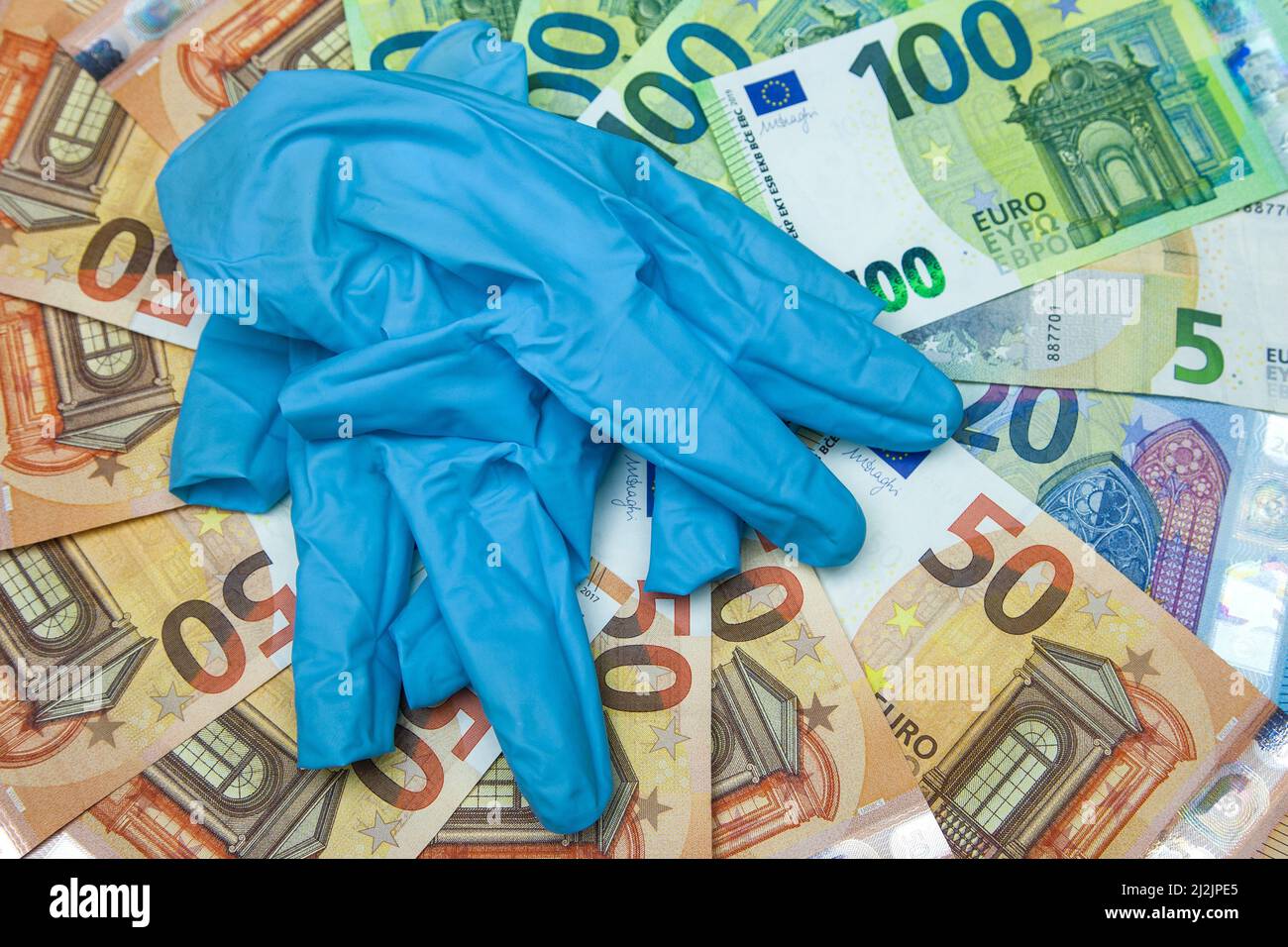 Gebrauchte Einweghandschuhe liegen auf Euro-Banknoten. Was kostet uns die Corona-Pandemie und wie sollen wir dafür bezahlen? Stockfoto