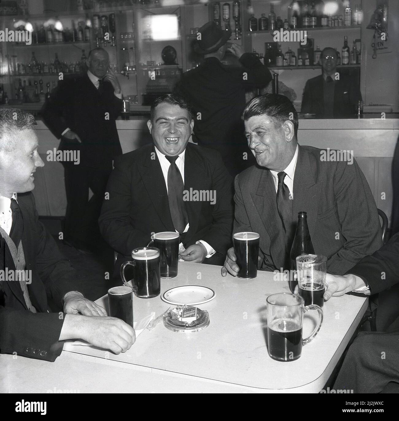 1950s, historisch, ein Bier fließt, während drei Stahlarbeiter in Jacke und Krawatte einen Drink und ein Lachen im Works Social Club bei einer Unternehmensfunktion, Steel Company of Wales, Abbey Works, Port Talbot, Wales, Großbritannien, genießen. Stockfoto