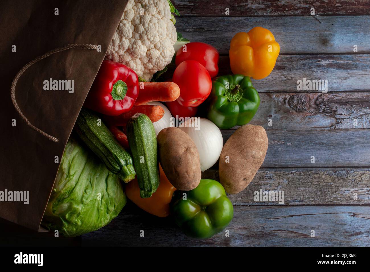 Eine recycelte Papiertüte aus dem Lebensmittelgeschäft voller Gemüse, Konzept der gesunden Ernährung auf einem hölzernen Vintage-Tisch Stockfoto