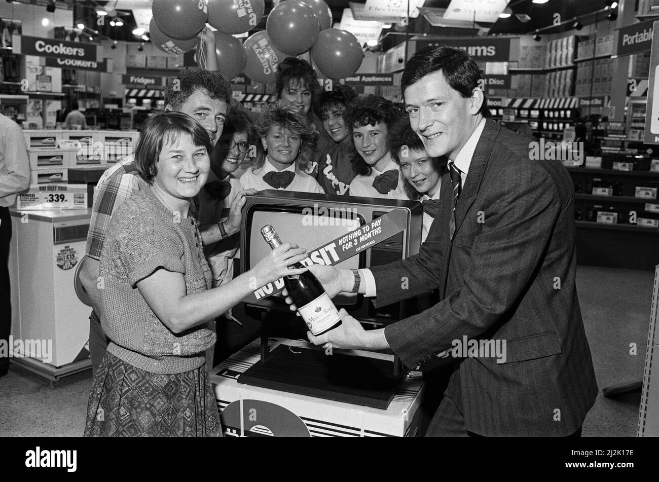 Champagnershoppen - Mrs Winifred Haigh und ihr Mann Jack (links) waren die ersten von 50 Kunden, die kostenlose Flaschen Champagner bekamen, nachdem sie £200 oder mehr im neuen Currys-Elektrosuperstore von Huddersfield ausgegeben hatten. Die Übergabe erfolgt durch Herrn Hamish Allan, Manager des Stores auf dem Ringway Industrial Estate, Beck Road, der von anderen Mitarbeitern beobachtet wird. 2.. Oktober 1987. Stockfoto