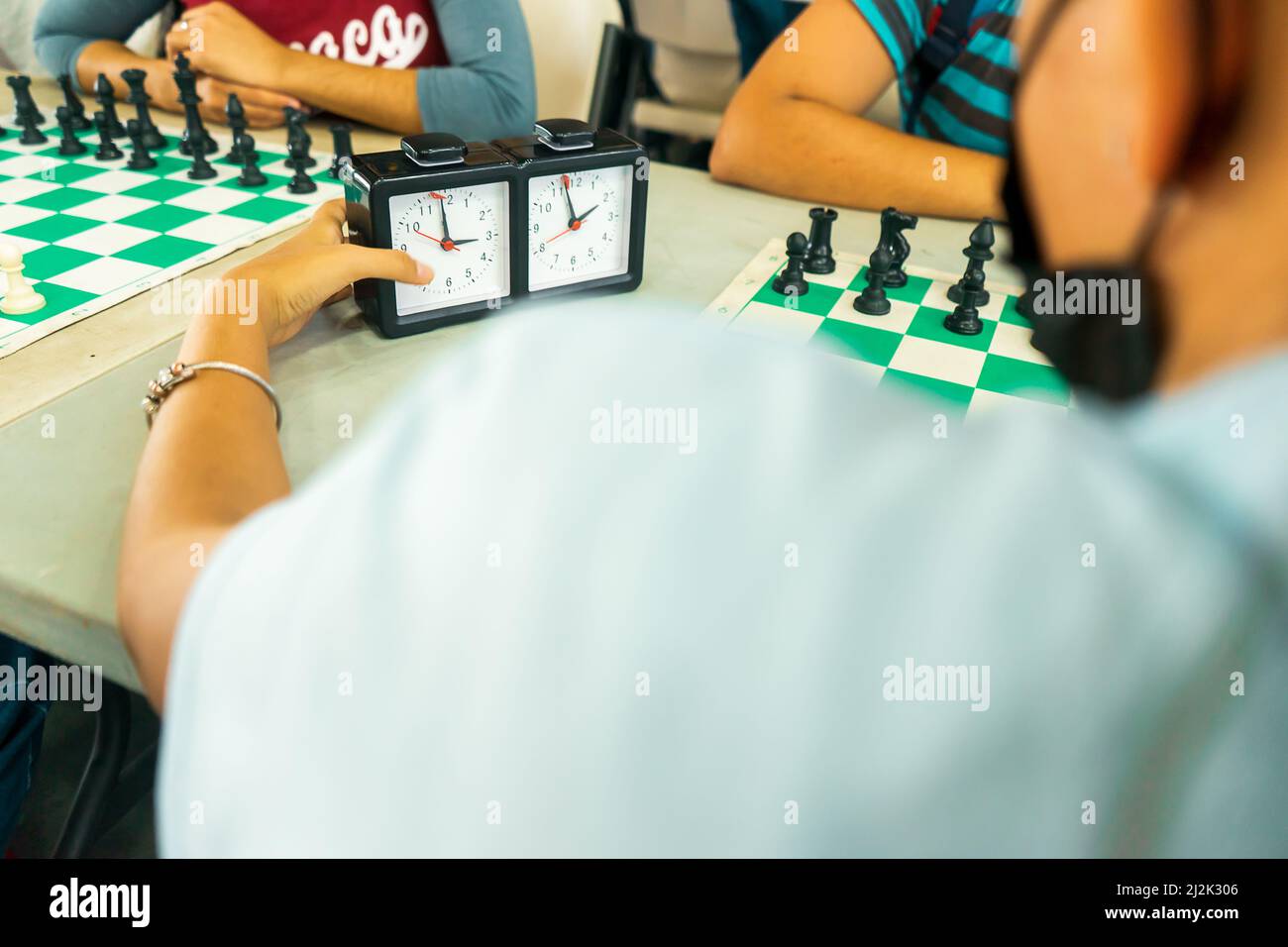 Nicht erkennbare junge lateinische Frau, die während eines Schachspiels die Uhr nimmt Stockfoto