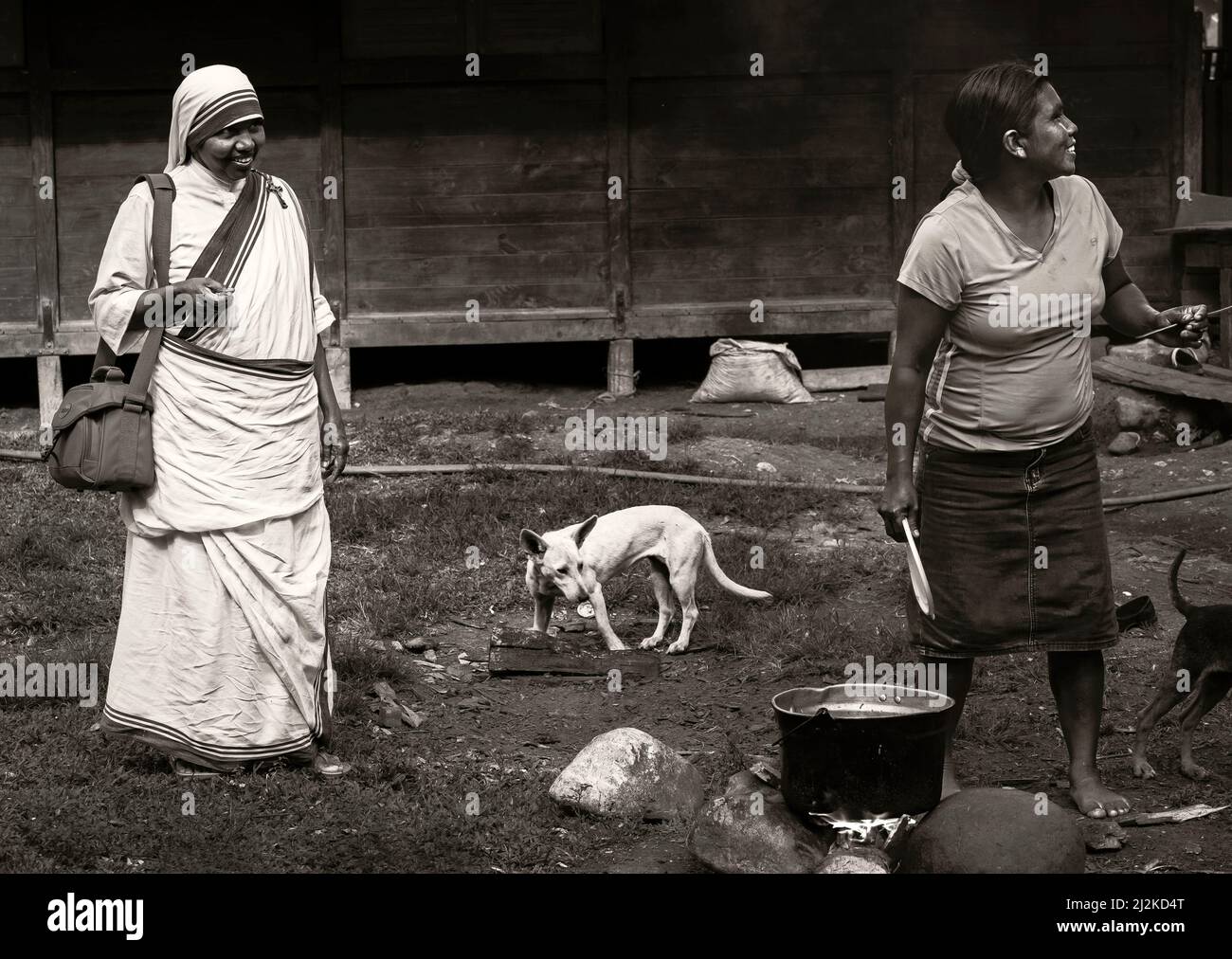 Cabecar indigene Frau, die auf offener Flamme kocht, während Mutter Teresa Schwester zuschaut Stockfoto
