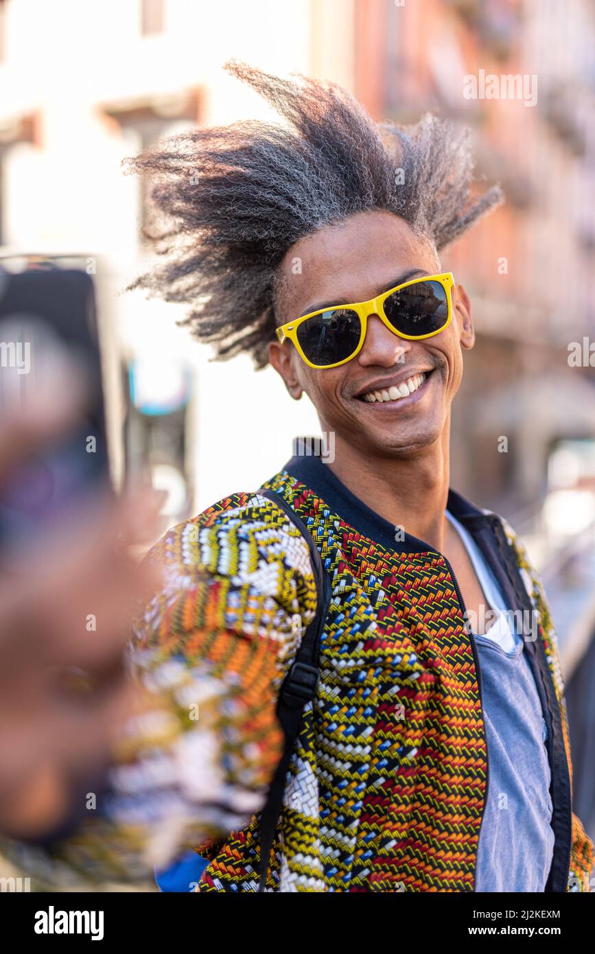 Hübscher junger Mann, der sein Smartphone für ein Selfie, lässige Kleidung und Street-Wear, coole Attitüde und afro amerikanische Mischvolk benutzt Stockfoto