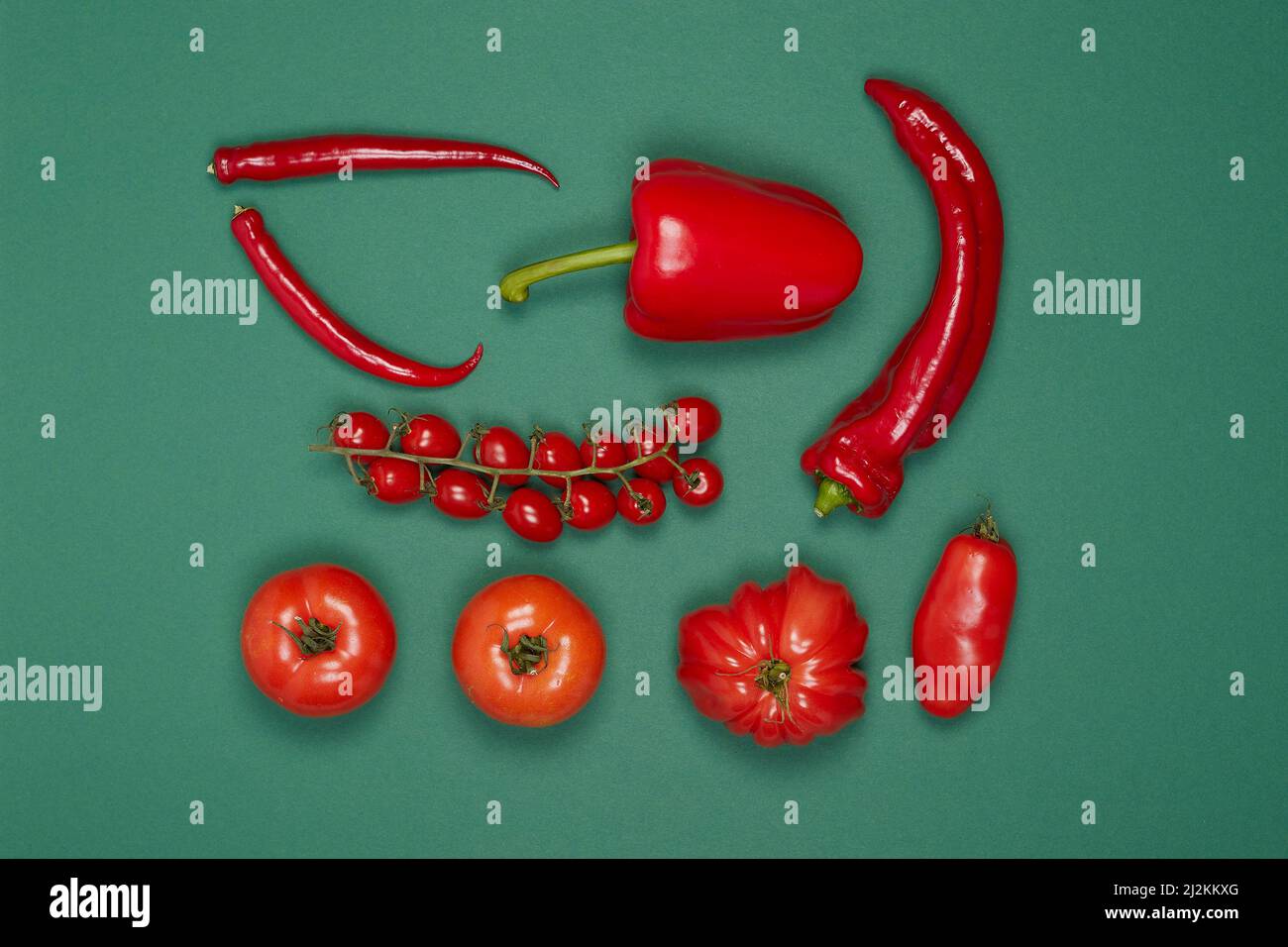 Gemüse in Gruppen mit roten Paprika, Pfefferoni und Tomaten auf grünem Hintergrund Stockfoto
