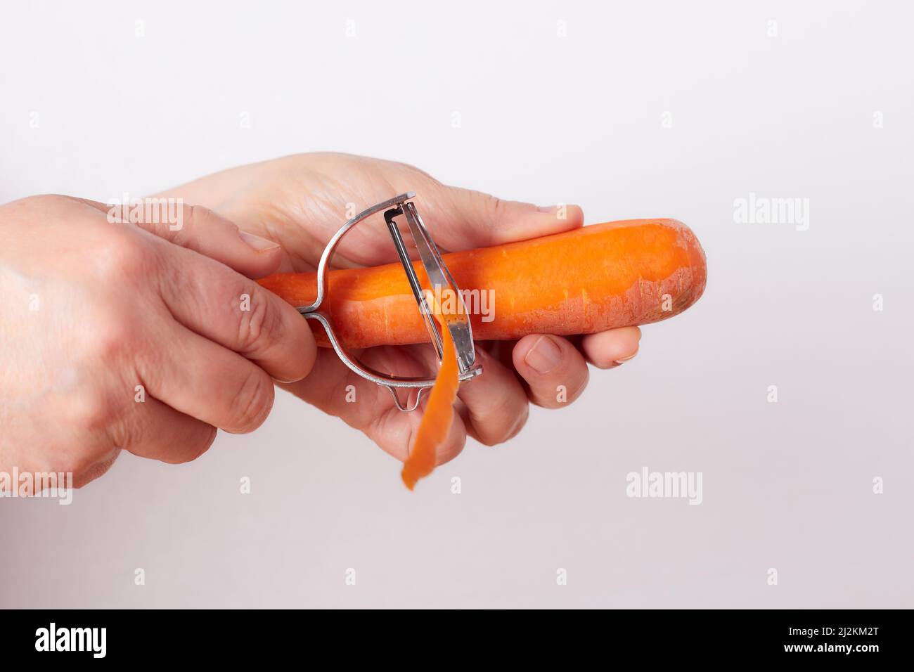 Die Hände der Frau entfernen die äußere Schicht einer Karotte mit einem Julienneschneider Stockfoto