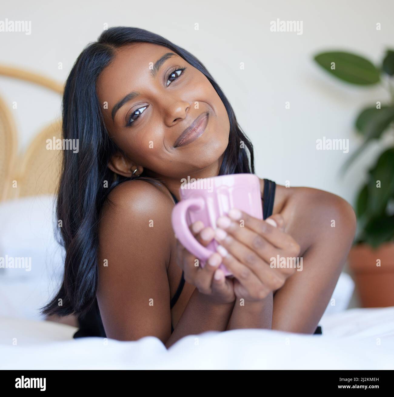 Eine frische Tasse Kaffee am Morgen. In voller Länge Porträt einer attraktiven jungen Frau, die eine Tasse Kaffee genießt, während sie auf einem Bett liegt. Stockfoto