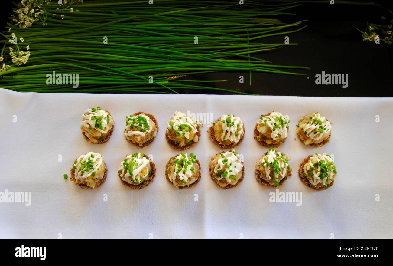 Skandinavische Eier und Matjes Hering auf dunklen Brotkanapés auf Tablett mit Schnittlauch und weißen Blüten Stockfoto