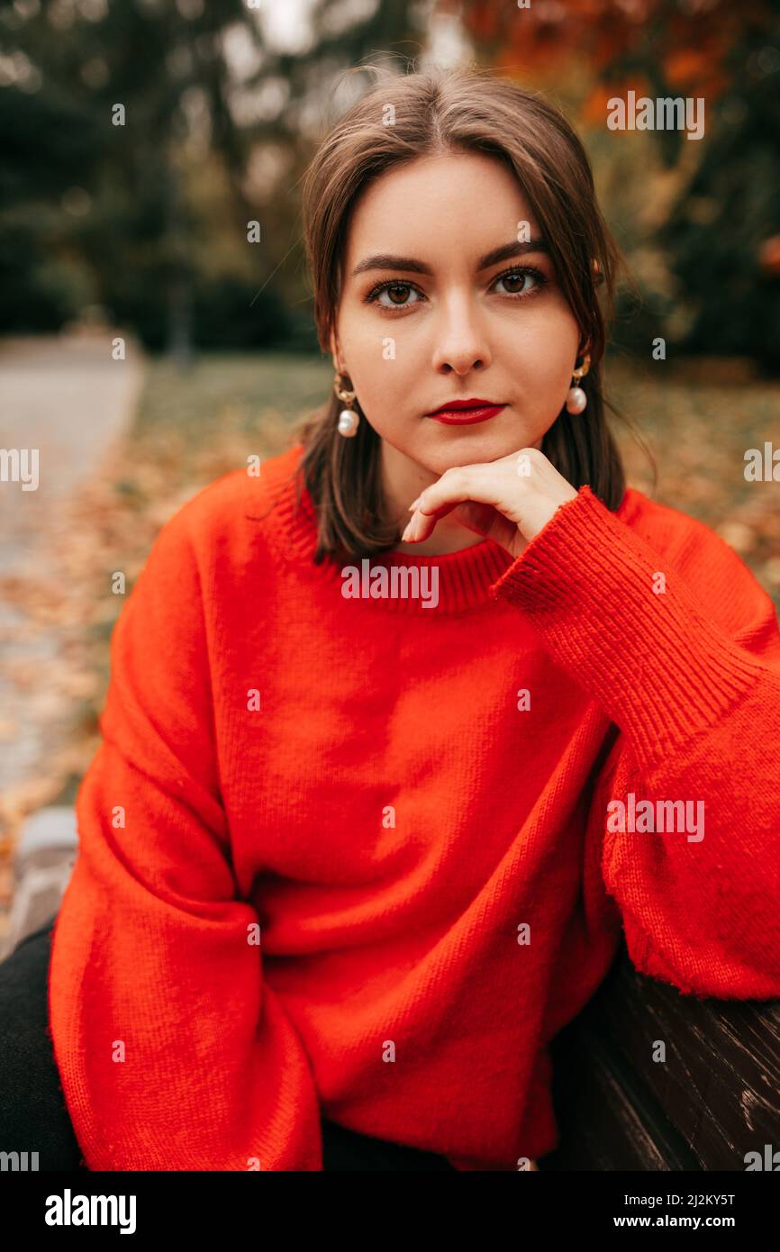 Portrait hübsche junge Frau, die sich an der Hand lehnt und im Herbstpark auf der Bank sitzt. Entspannend, die Natur besinnend Stockfoto