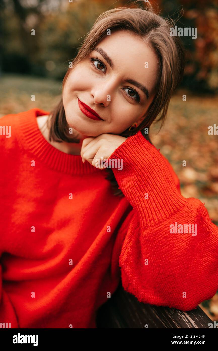 Vertikales Porträt schöne junge Frau, die Hand gelehnt, sitzt auf der Bank im Herbstpark. Entspannend, die Natur besinnend Stockfoto
