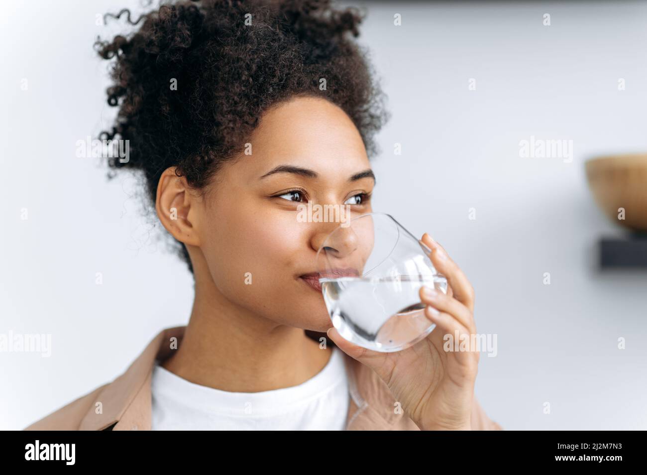 Gesundes Lifestyle-Konzept. Die hübsche afroamerikanische junge Frau trinkt zu Hause ein Glas Wasser. Schöne glückliche gesunde Mischrasse Mädchen folgen gesunden Lebensstil, trinken Sie die tägliche Menge an Wasser Stockfoto