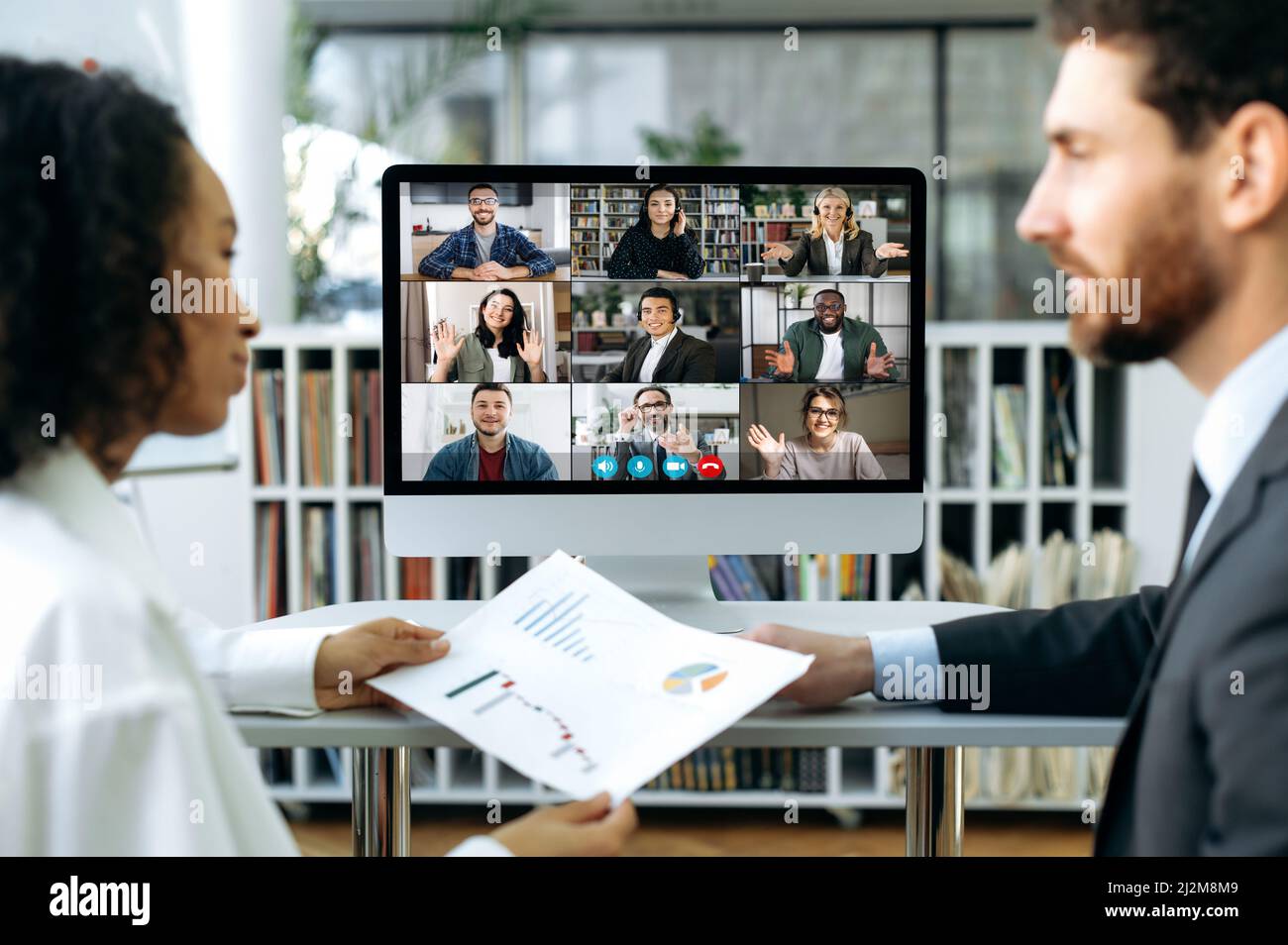 Eine internationale Gruppe von Geschäftspartnern traf sich zu einem Online-Video-Meeting. Geschäftskollegen, ein Mann und eine Frau sitzen im Büro vor einem Computerbildschirm und studieren gemeinsam Geschäftspapiere Stockfoto