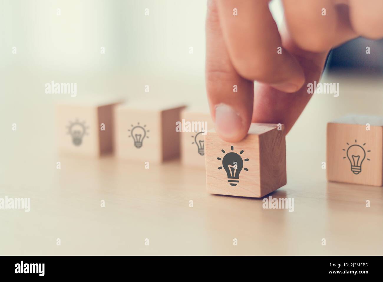 Idee und Kreativität Konzept. Männliche Hand hält Holzwürfel mit Glühbirnen Symbol auf hellem Hintergrund. Teamwork Brainstorming Ideen, Bewertung und Selec Stockfoto