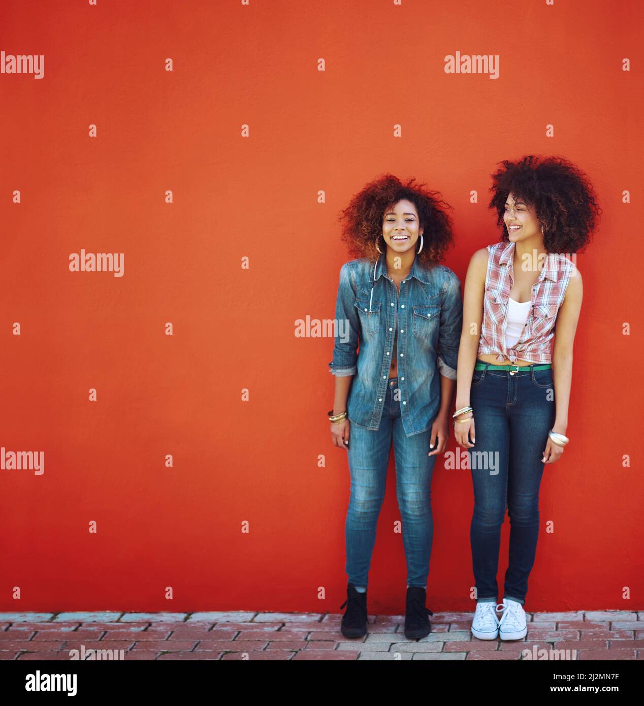 So froh, dass ich sie in meinem Leben habe. Aufnahme von zwei jungen Freunden, die vor einer roten Wand posieren. Stockfoto