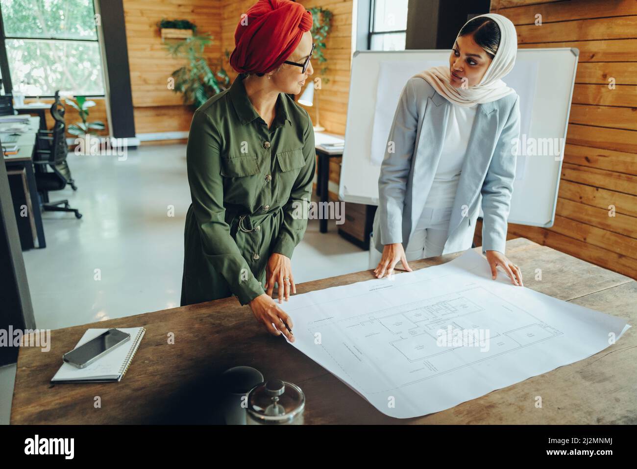 Muslimische Designer diskutieren während der Arbeit mit einer Blaupause-Zeichnung. Zwei kreative Geschäftsfrauen planen ein innovatives Projekt. Weiblicher archit Stockfoto