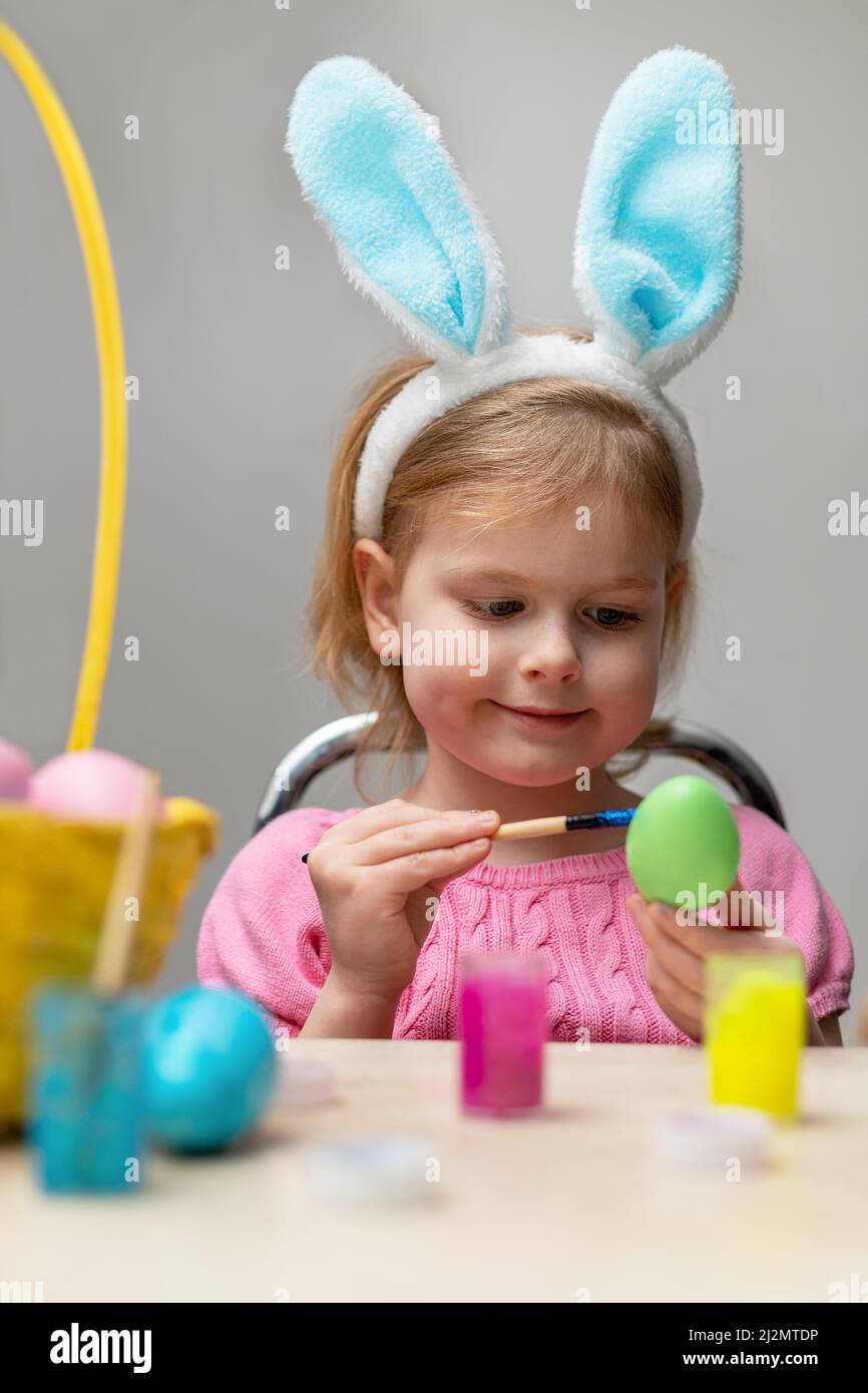 Kleine schöne Mädchen malen Ostereier. Kinder tragen Osterhasen Ohren. Urlaubsvorbereitungen. Stockfoto