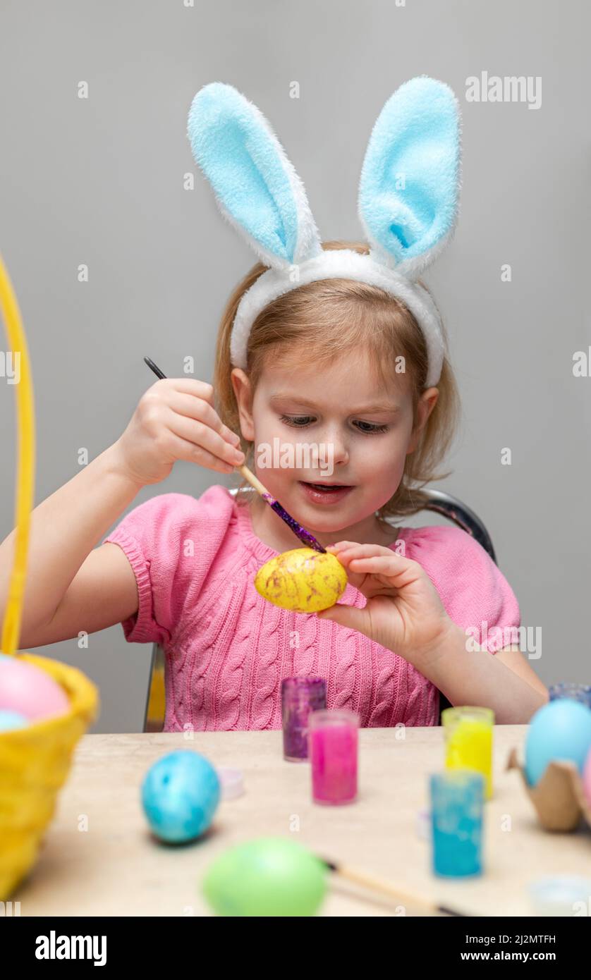 Lächelndes kleines Mädchen, das Ostereier malt. Kind trägt Osterhasen Ohren. Urlaubsvorbereitungen Stockfoto